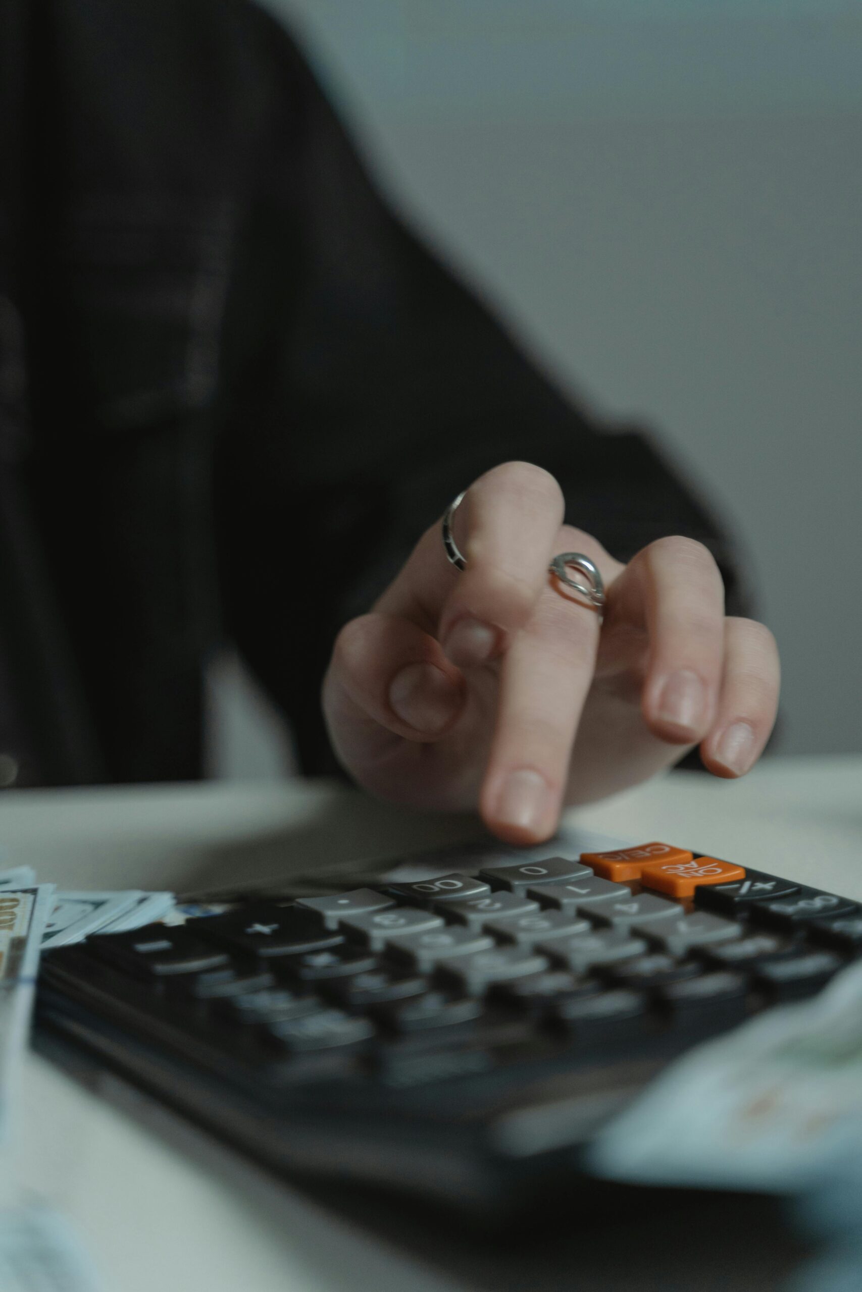 Person's hand with a ring presses calculator keys while money lies nearby, suggesting budgeting or accounting.